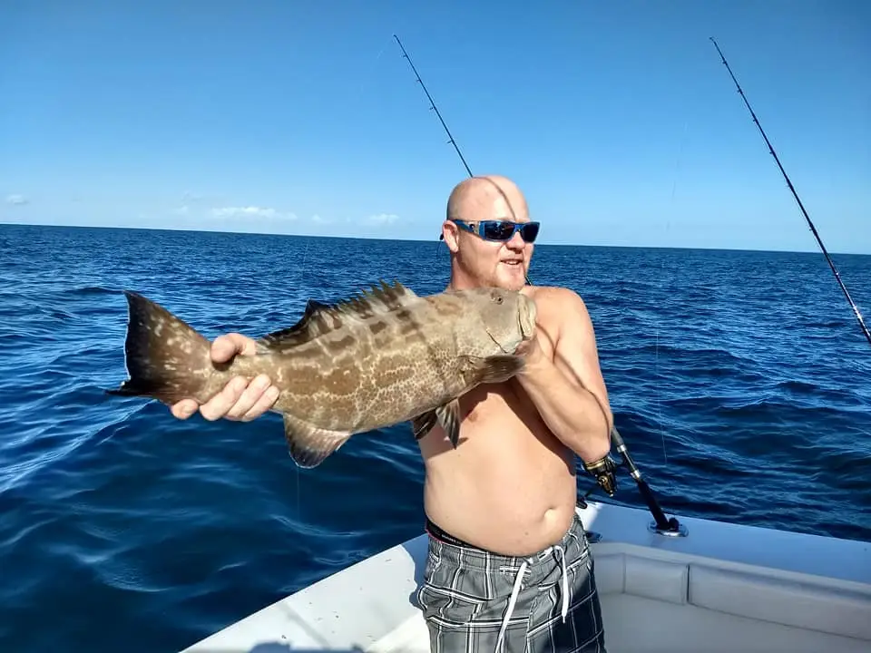 Angler holding a large grouper on the deck of an offshore fishing boat