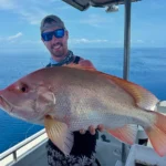 Angler from Akula Sportfishing in Port Douglas holding a snapper-like fish on a boat