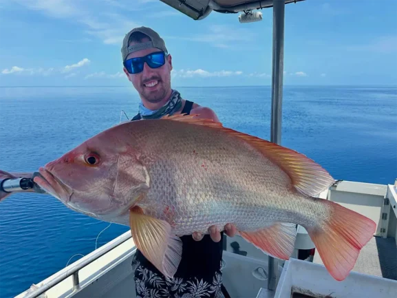 Angler from Akula Sportfishing in Port Douglas holding a snapper-like fish on a boat