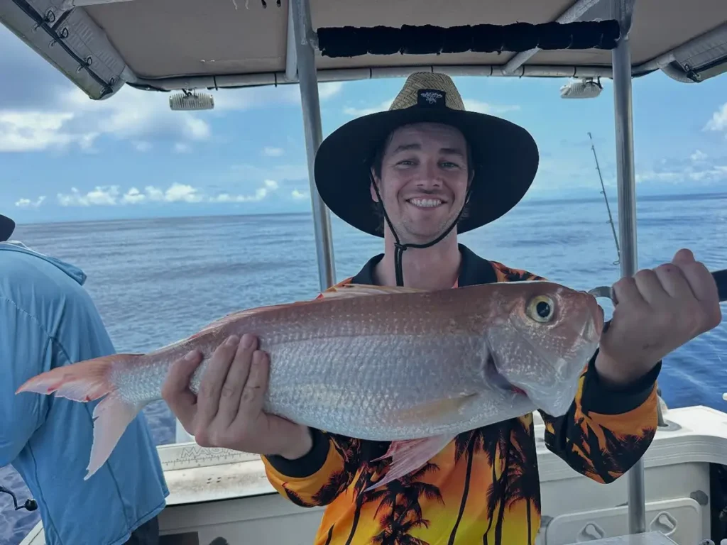 Smiling angler from Akula Sportfishing in Port Douglas holding a snapper-like fish on the boat