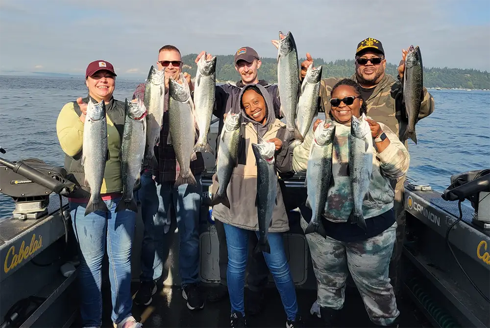 Group of anglers holding freshly caught salmon aboard an All Star Seattle Fishing Charters boat in Puget Sound.