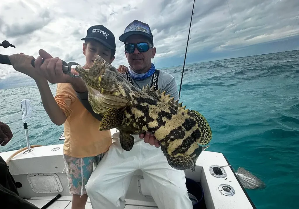 Two anglers holding a large jewfish on a boat