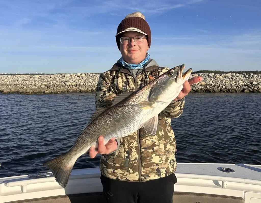 young angler holding a fish on a boat with a rock jetty in the background