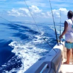 Person standing on a boat with trolling lines trailing behind it