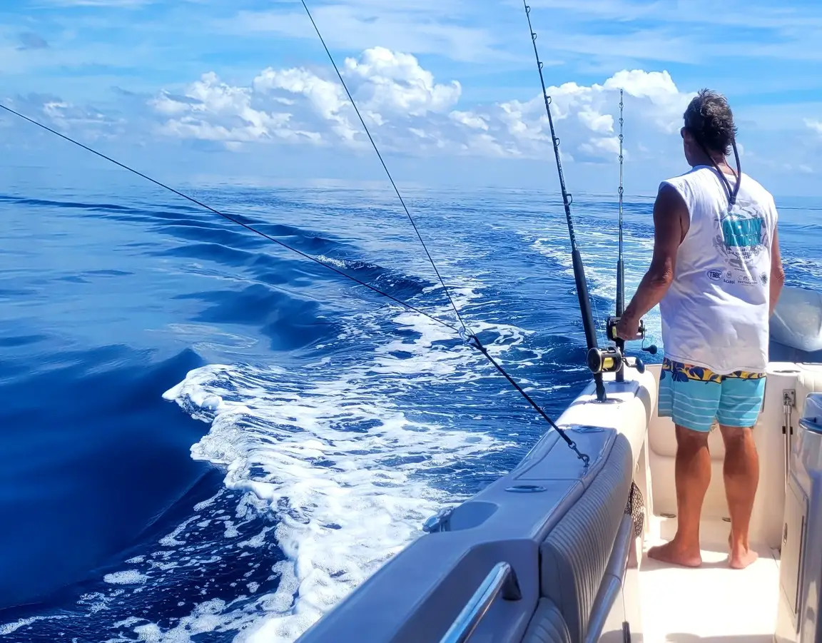 Person standing on a boat with trolling lines trailing behind it