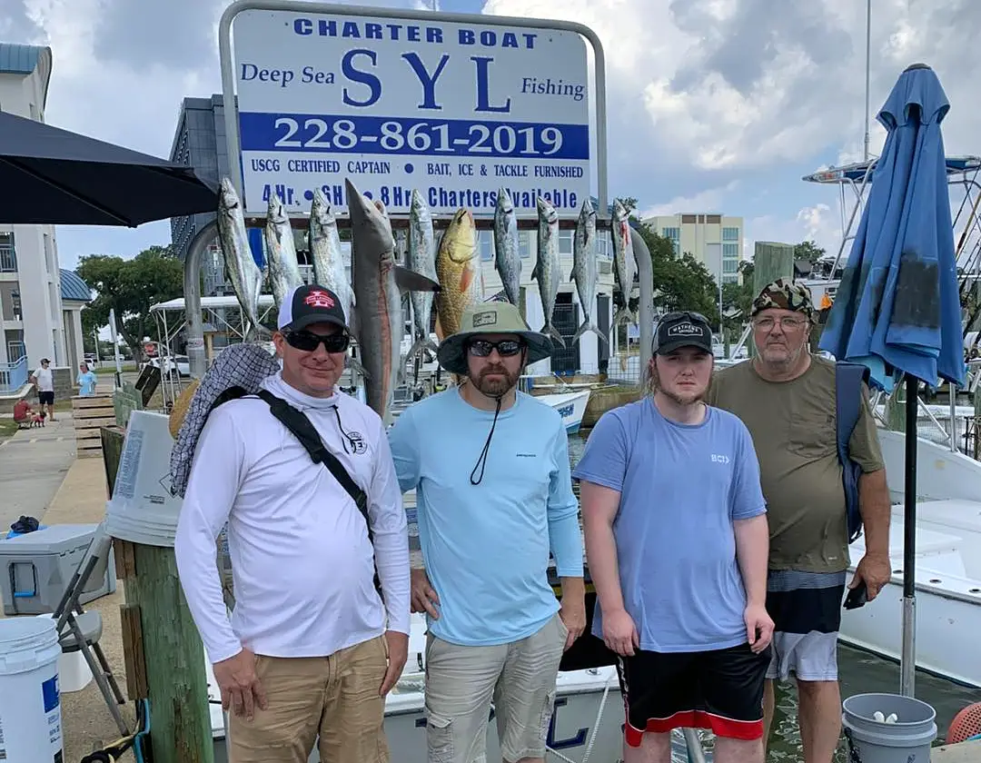 group of four anglers standing in front of a hanging fish display at a marina