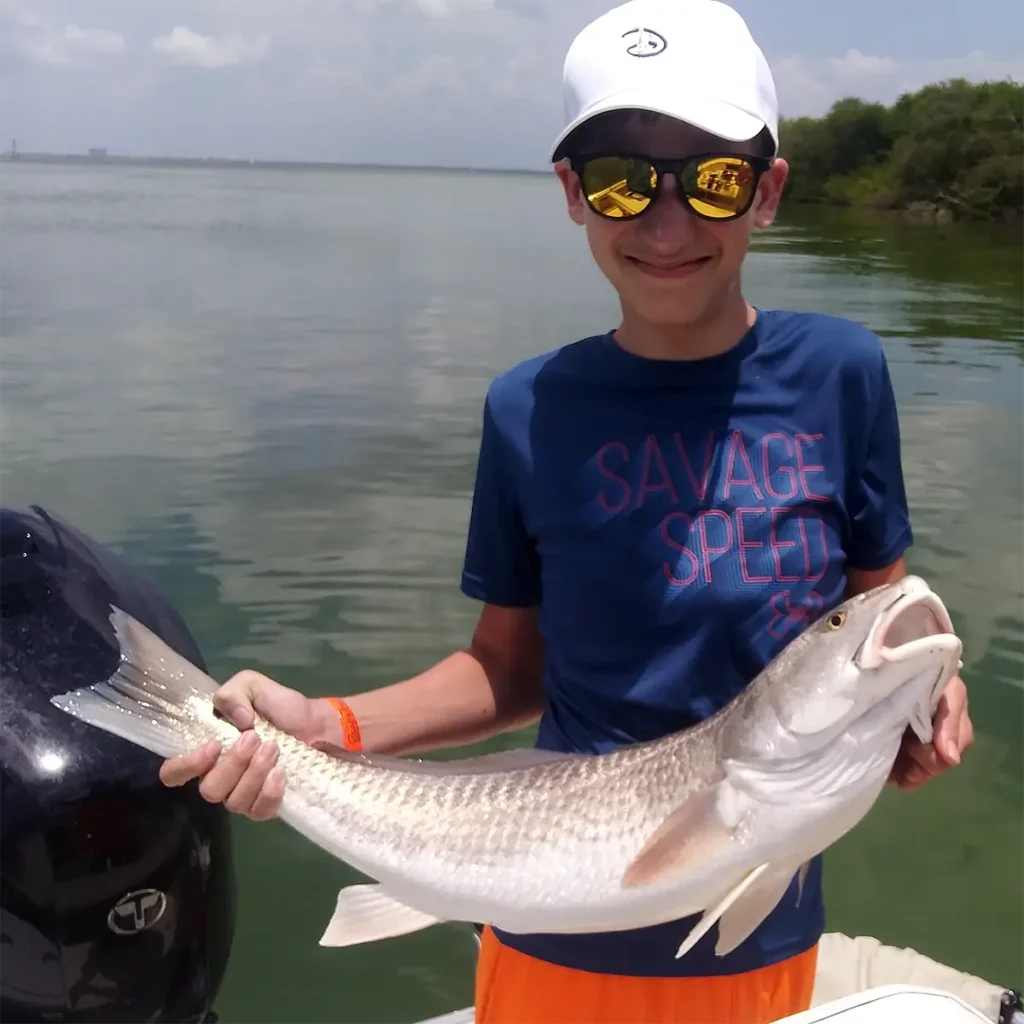 boy holding a redfish on a boat with calm Tampa Bay water behind him