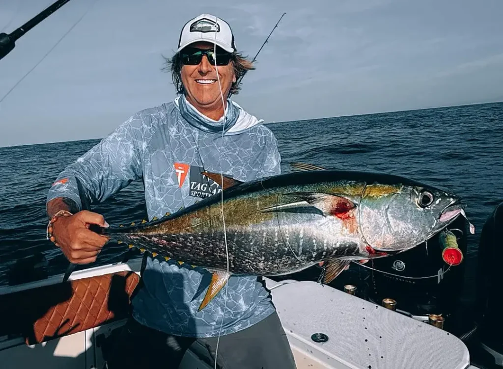 Angler sitting on boat deck holding a large yellowfin tuna offshore Cabo San Lucas