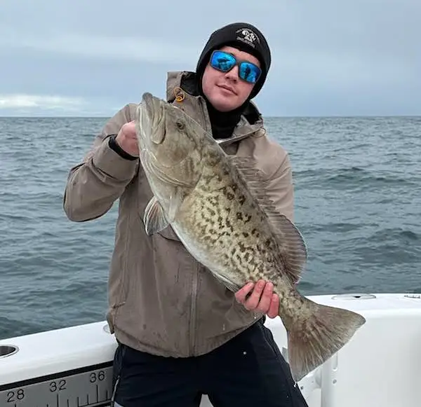 angler holding a large bottom fish on a boat over open water