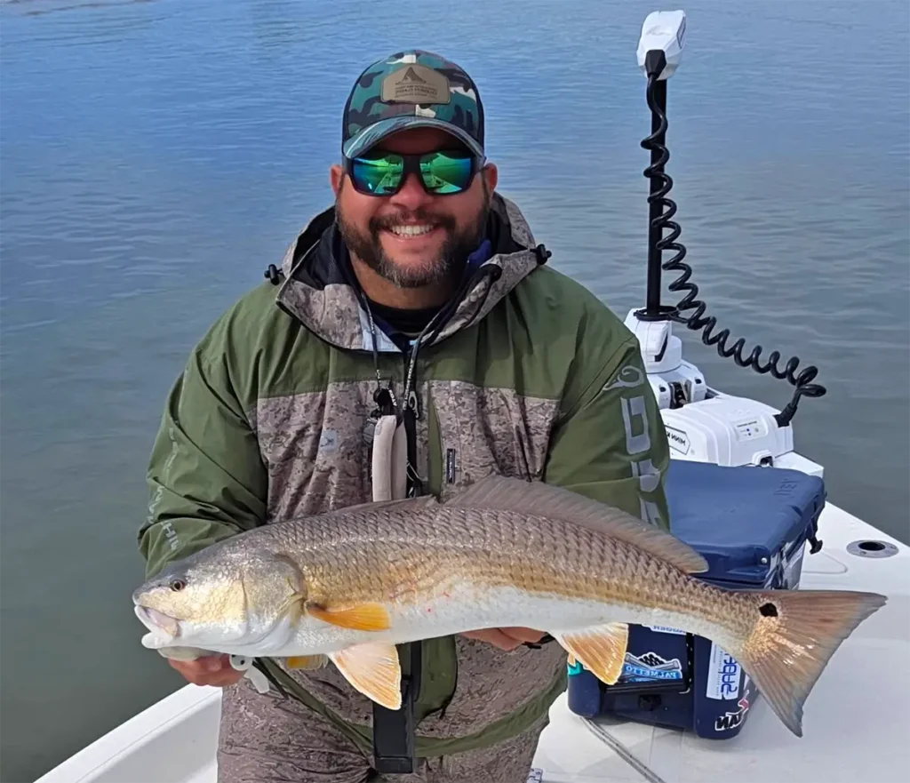 angler holding a bronze-colored fish on a boat with calm water behind