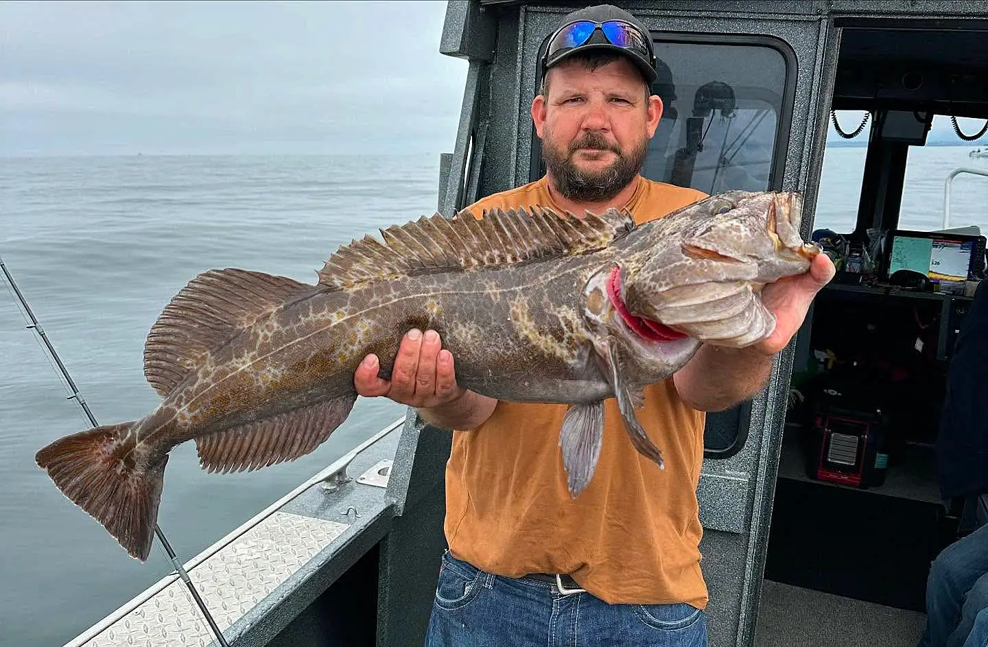 Angler holding a large lingcod on a Crescent City Fishing charter boat