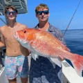 man holding a red snapper on a fishing boat with another man standing nearby