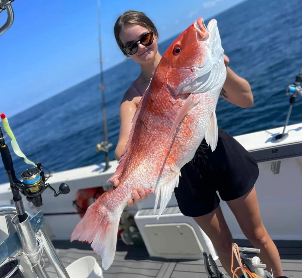 woman holding a red snapper on a fishing boat with open water in the background