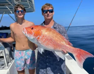 man holding a red snapper on a fishing boat with another man standing nearby