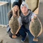 Two people kneeling indoors holding two flounder