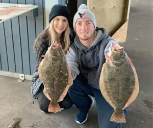 Two people kneeling indoors holding two flounder