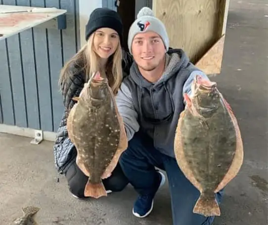Two people kneeling indoors holding two flounder