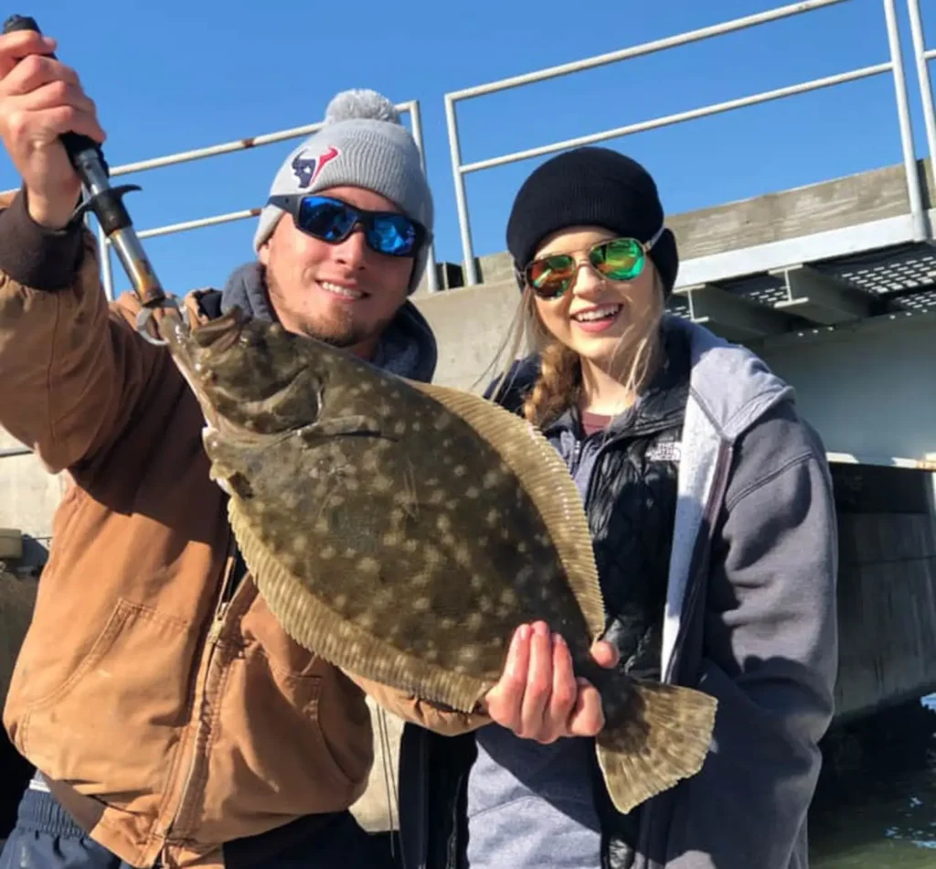 Two anglers holding a flounder with a fish gripper