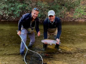 Two anglers standing in a shallow stream holding a rainbow trout