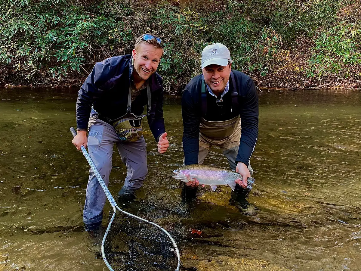 Two anglers standing in a shallow stream holding a rainbow trout