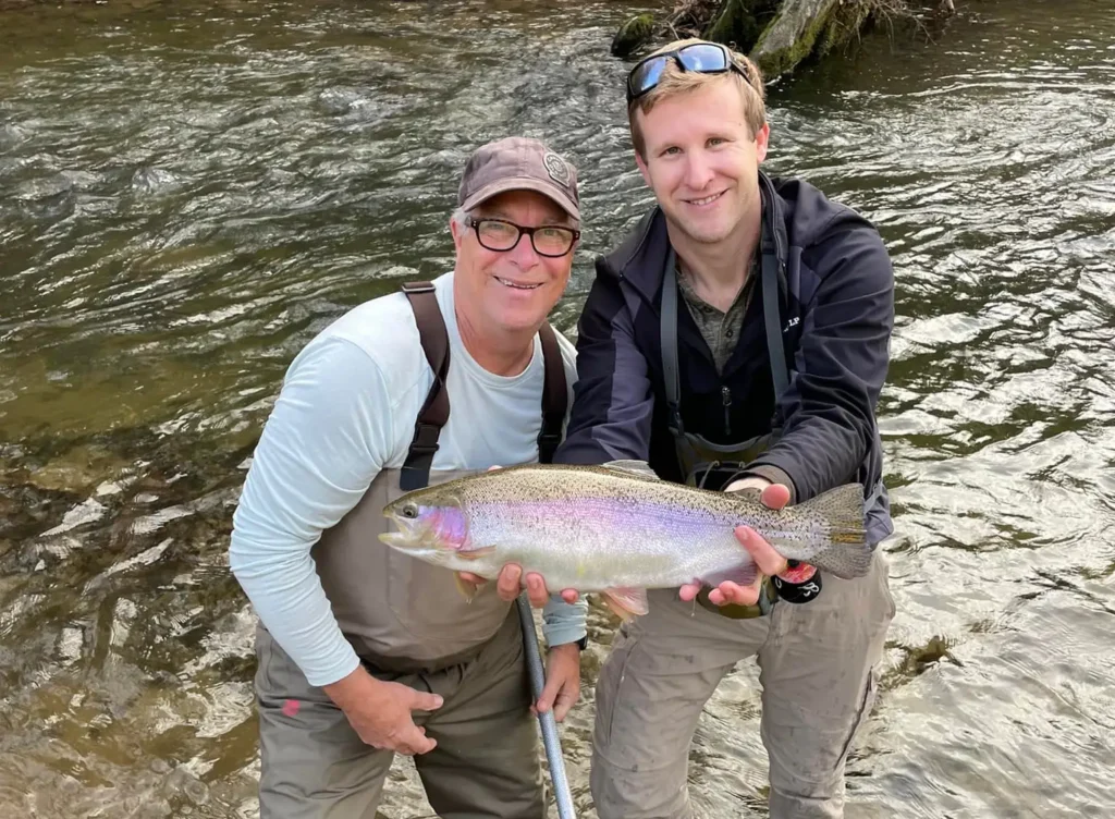 Two anglers holding a rainbow trout in moving river water