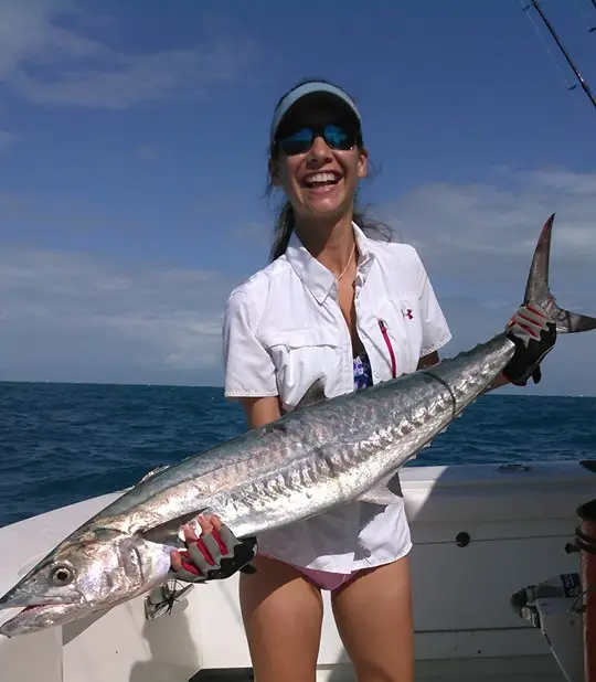 Woman holding a large kingfish on a boat in calm ocean water
