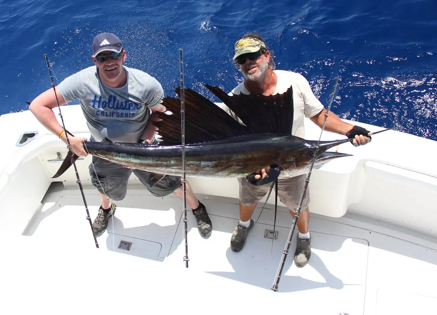 Two anglers holding a large sailfish on a boat in blue offshore water