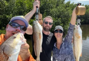 group of men and a woman holding redfish using handheld hooks