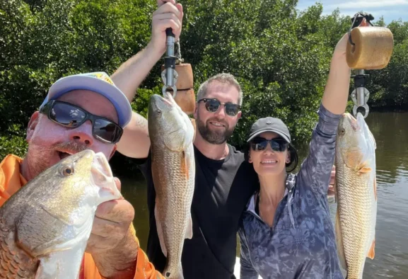 group of men and a woman holding redfish using handheld hooks