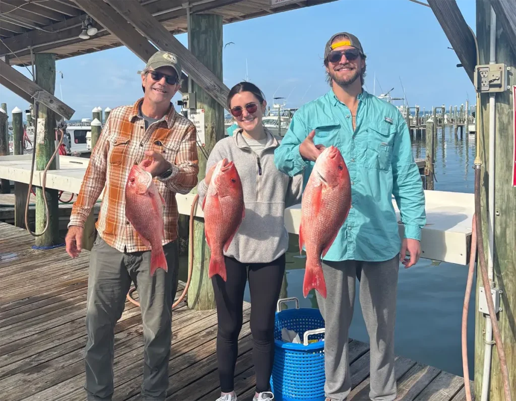 Three anglers holding red snapper on a dock near Gulf Shores Alabama