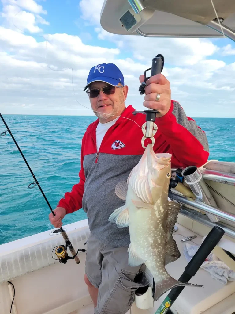 angler holding a light-colored bottom fish beside a boat over calm blue water