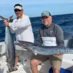 Two anglers holding large wahoo on a boat