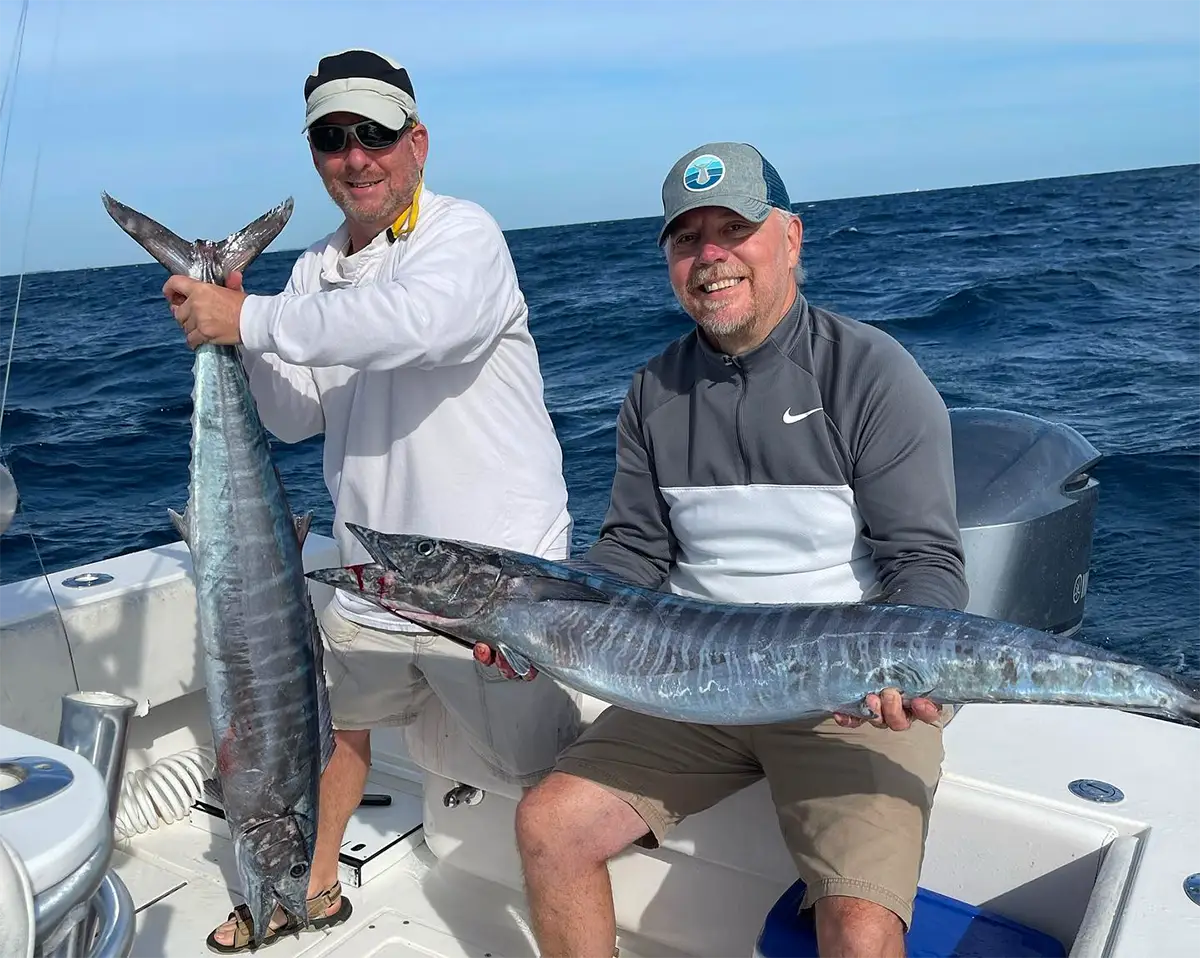 Two anglers holding large wahoo on a boat