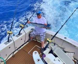angler holding a long fish on the back deck of a sportfishing boat with blue water behind