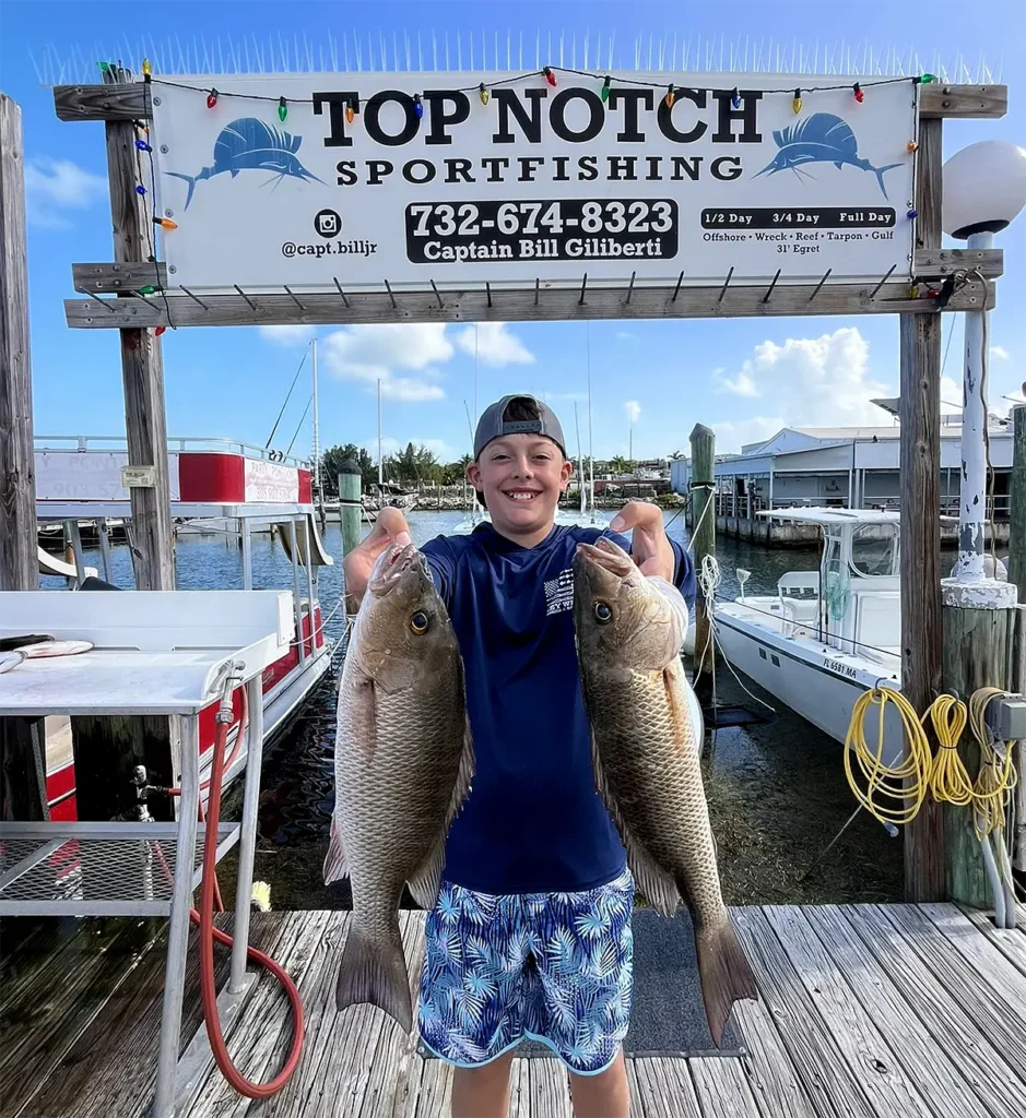 Young angler holding two reef snapper at a Marathon Florida dock after a trip with Top Notch Sportfishing