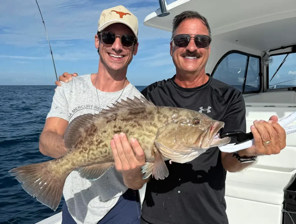 Two anglers holding a large grouper on an offshore fishing boat near Naples Florida