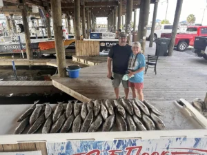 two adults standing behind a large display of fish at a dockside cleaning station