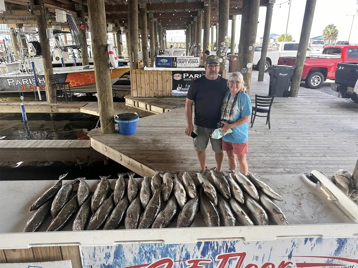 two adults standing behind a large display of fish at a dockside cleaning station