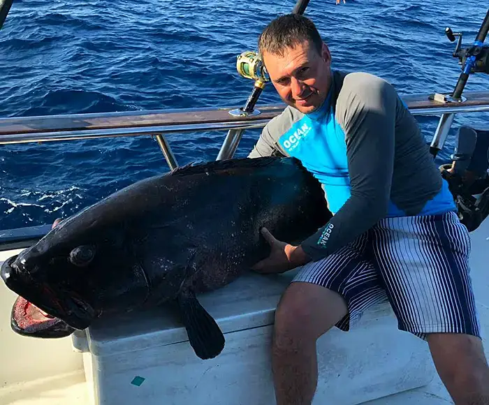 Angler on a Phuket fishing charter holding a large deep water grouper at the rail