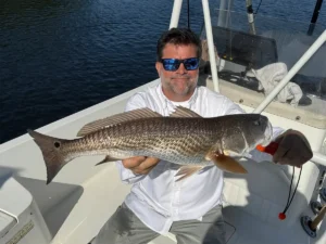 man holding a redfish on a boat in bright daylight