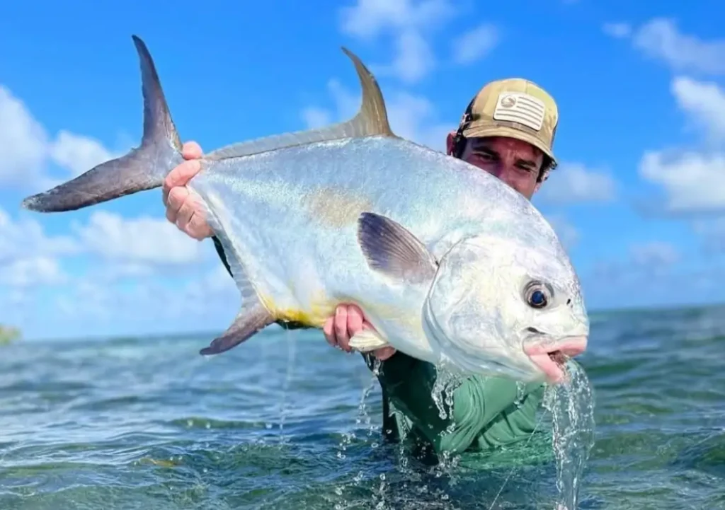 angler holding a large permit in shallow water near San Pedro Belize