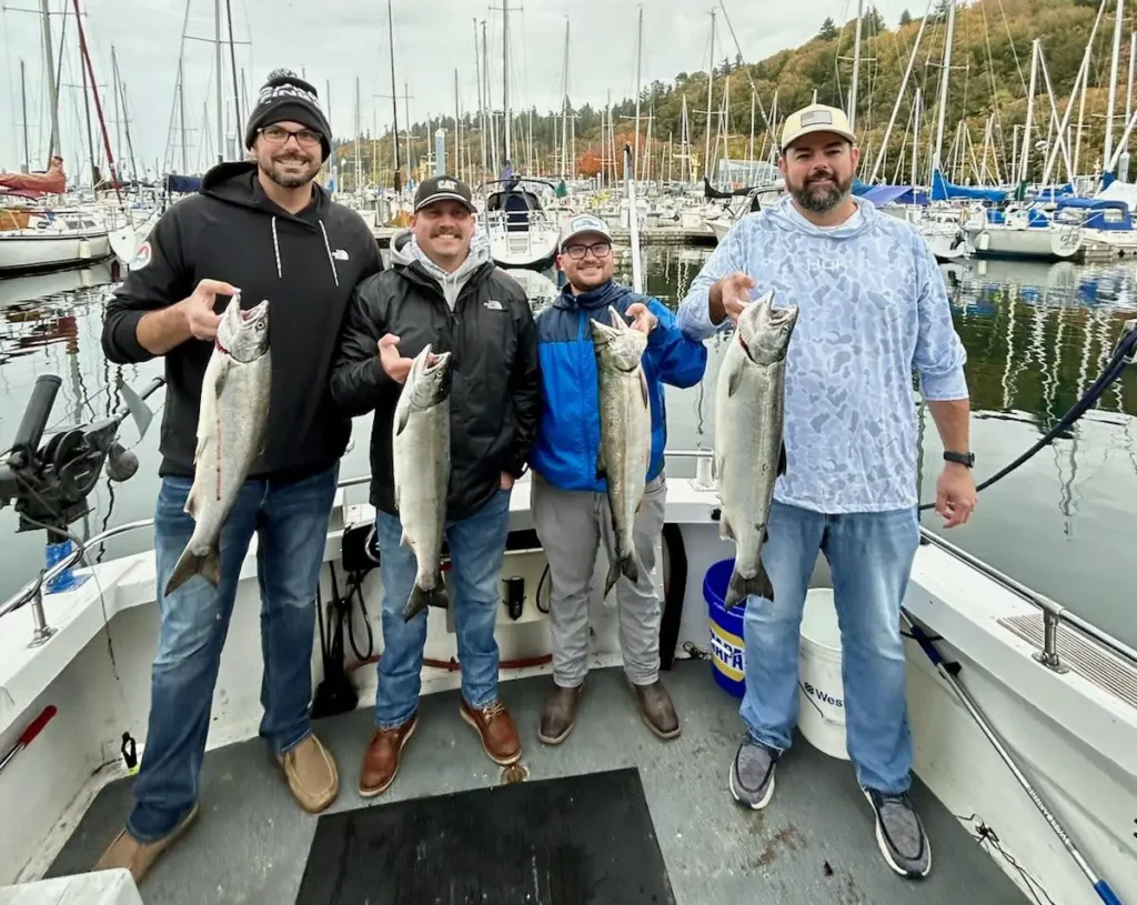 Four anglers holding salmon at a marina after a successful Seattle fishing charter.