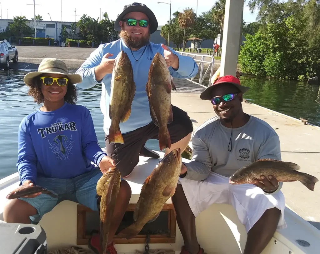 three men holding several grouper while sitting on a boat at a dock in Tampa Bay
