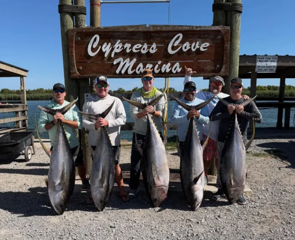 Group of anglers standing in front of a Cypress Cove Marina sign holding large tuna on the dock