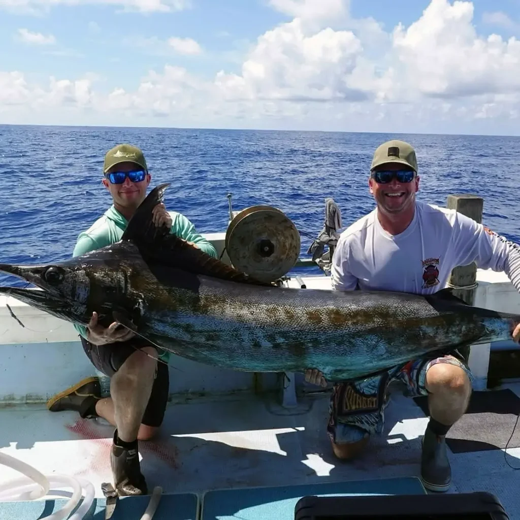 Two anglers holding a marlin on an offshore fishing boat